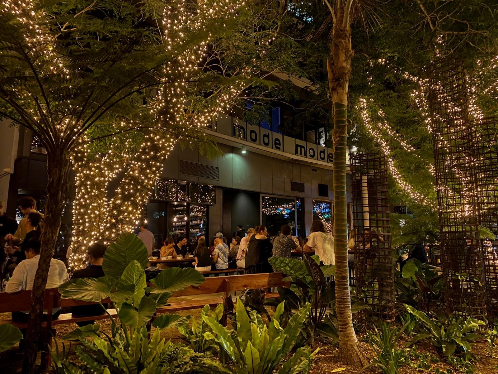Guests at long tables on Snack Man's East Street terrace beneath palms and trees wrapped in fairy lights